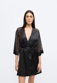 Mustast satiinist hommikumantel pitsist varrukatega, vöökohal lipsuga ja sügava V-kaelusega. Omab siledat tekstuuri ja põlvekõrgust lõiget.