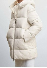 Světlá béžová prošívaná bunda s kapucí, opatřená předním zipem a dvěma bočními kapsami. Tkanina působí hladce s prošívaným vzorem.
