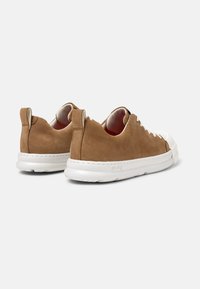 Zapatillas de ante marrón con suela de goma blanca, puntera redonda, detalles de cordones en contraste y pestañas en la parte posterior. Textura suave.