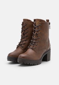 Brune skinn ankelstøvler med høy blokkhel, snøring foran og glidelås på siden. Grov såle med mønsterdetaljer, med subtile sømaccents.