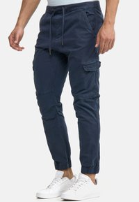 Granatowe spodnie cargo z sznurkiem w talii, wyposażone w elastyczne mankiety, boczne kieszenie i gładką, trwałą tkaninę.