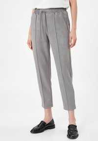 Pantalones gris claro, ajustados y fabricados con una tela suave y lisa. Presentan una cinturilla elástica con cordón y costuras laterales en contraste.