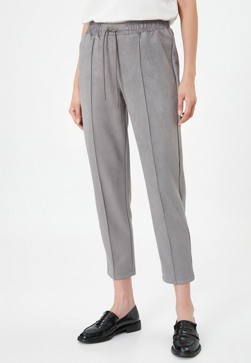 Pantalones gris claro, ajustados y fabricados con una tela suave y lisa. Presentan una cinturilla elástica con cordón y costuras laterales en contraste.