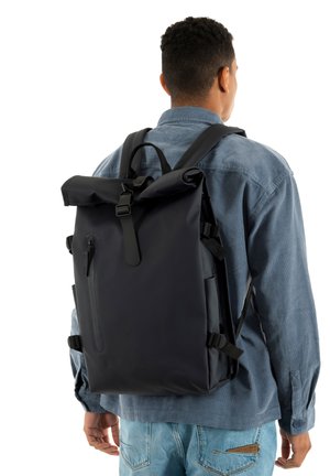 Musta vedenpitävä rullattava reppu säädettävillä remmeillä, etutaskulla ja tyylikkäällä muotoilulla, esitettynä henkilön päällä.