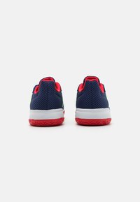 Zapatillas deportivas de malla en azul marino con acentos rojos, entresuela blanca y suela de goma texturizada. Presentan un collar y un talón acolchados para mayor comodidad.