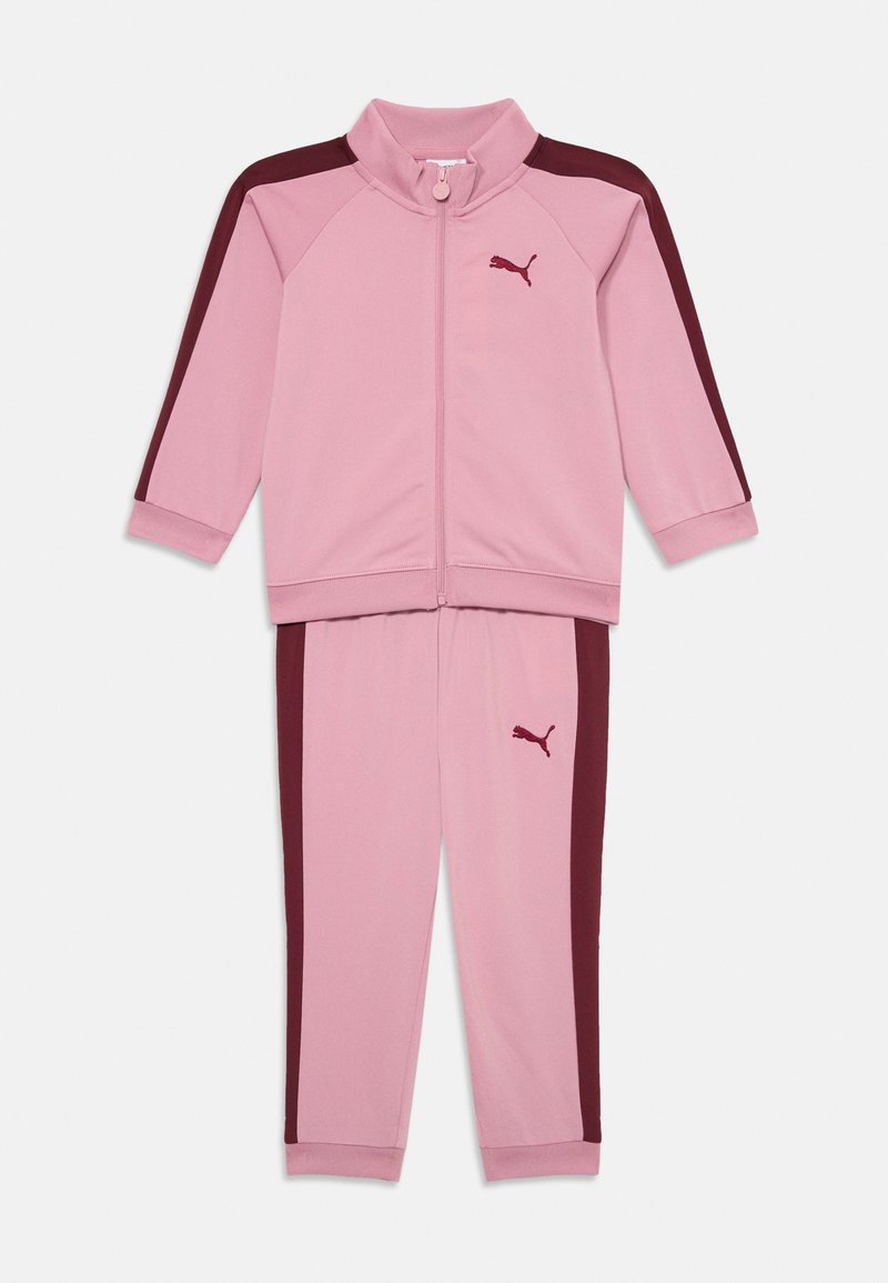 Roze trainingspak bestaande uit een ritssluitende jas met bordeauxrode accenten en bijpassende broek, gemaakt van een gladde stof met elastische manchetten.