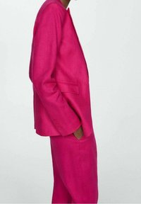 Fuchsia linnen pak met een getailleerd jasje en bijpassende broek. Het jasje heeft een smalle pasvorm en twee zijzakken.