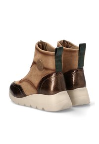 Botines de ante marrón claro con acentos metálicos marrones, suela gruesa blanca y pestañas verdes en la parte trasera para poner y quitar fácilmente. Detalle de logo circular presente.