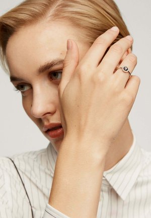 Anillo de plata con una piedra negra circular, usado en un dedo, mano posicionada cerca de la cara, mostrando piel suave y finos detalles del anillo.