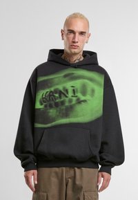 Sudadera negra con un gran estampado gráfico verde en el pecho. Presenta un bolsillo canguro y puños de canalé. Fabricada con tejido suave.