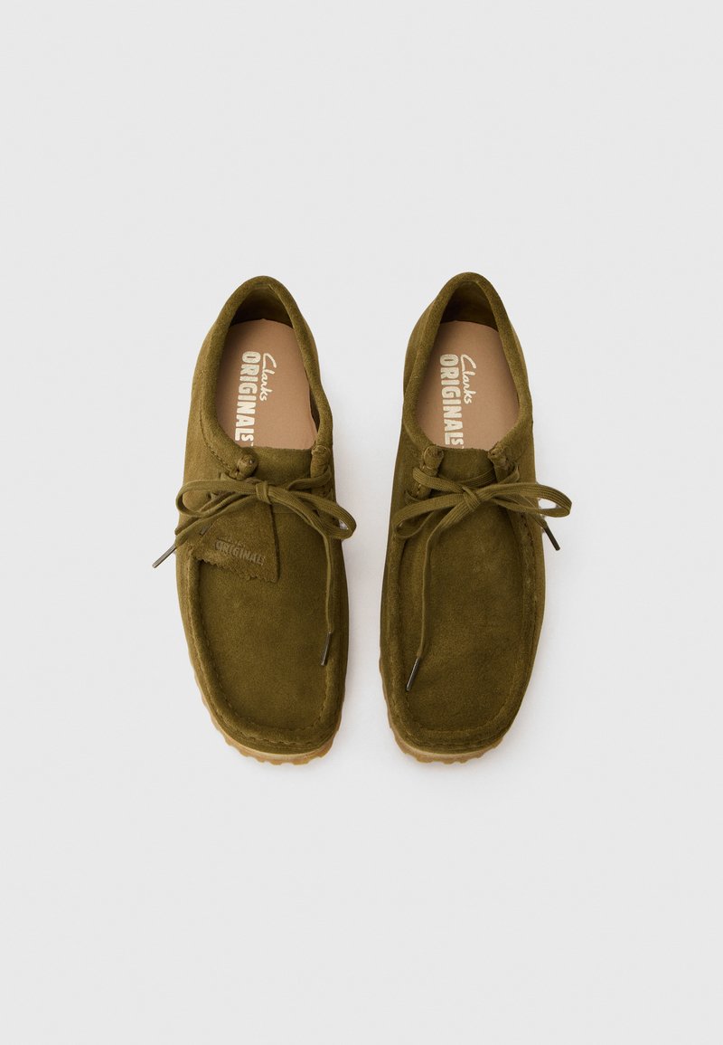 Zapatos de ante verde con cordones, puntera redonda, suela de goma y diseño minimalista, que cuentan con una etiqueta con la marca "Clarks Originals".
