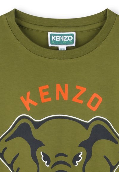 T-shirt en coton vert olive avec un col rond, présentant un graphique d'un éléphant sous le texte "KENZO" en gras orange avec des contours blancs.
