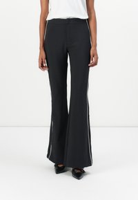 Black pants with a flared design, made from a smooth material. Features white side accents and a fitted waistband. Worn with black shoes.
