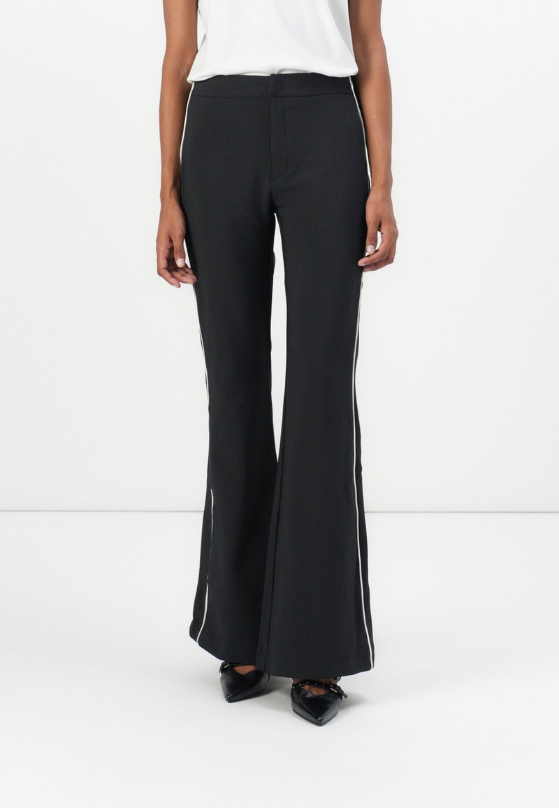 Black pants with a flared design, made from a smooth material. Features white side accents and a fitted waistband. Worn with black shoes.