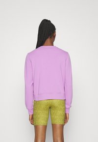 Sweat-shirt lilas avec un col rond et des poignets côtelés, associé à un short cycliste jaune texturé avec un motif subtil.