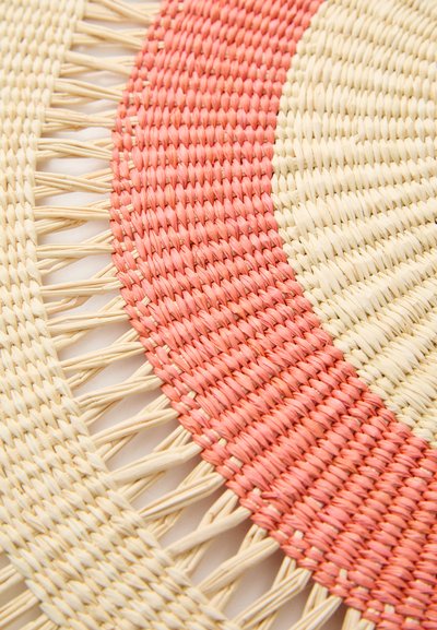 Round woven placemat featuring alternating sections of pale yellow and coral pink, with visible texture and intricate edge detailing.