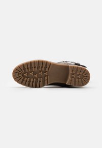 Suola in gomma marrone, con un motivo di battistrada robusto e marchio del brand. Presenta un leggero tacco e un'area della punta rinforzata.
