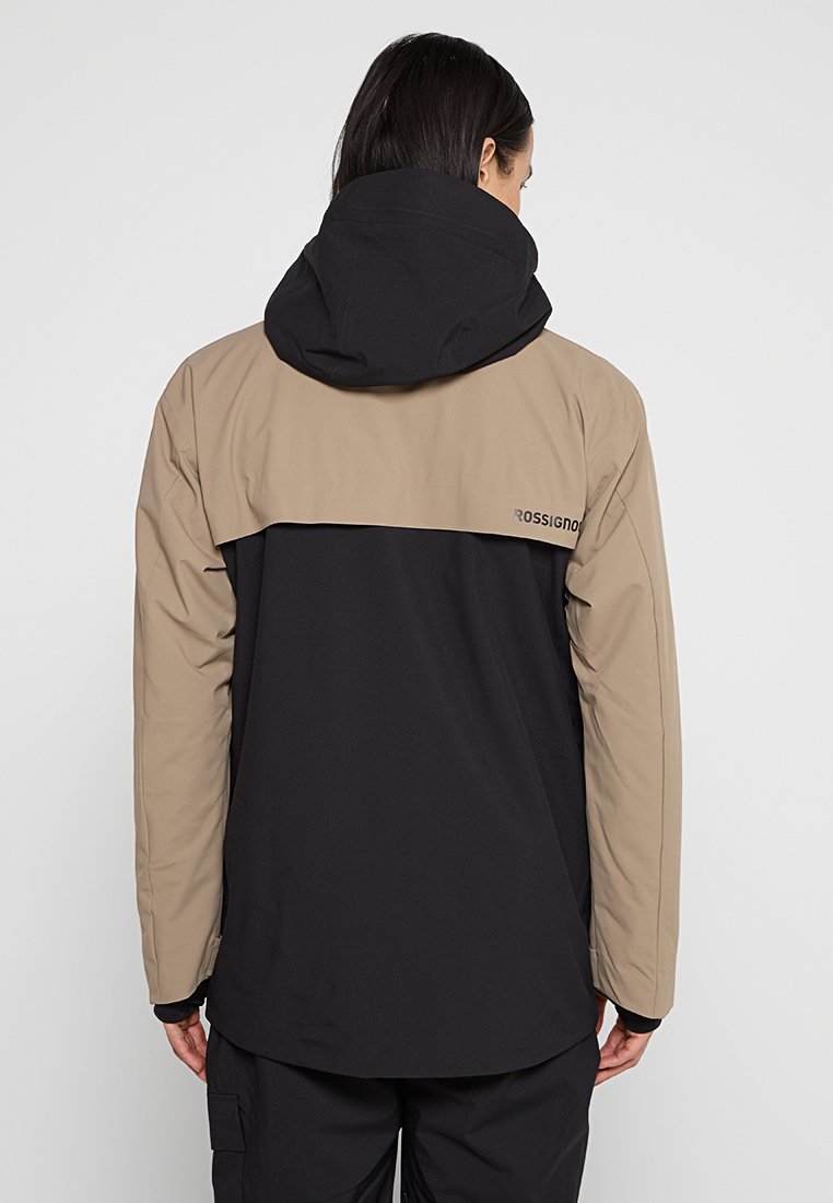 Schwarze und beige Jacke mit Kapuze. Glatte Textur, zweifarbiger Design, mit einem Logo auf dem Rücken. Lange Ärmel und lockere Passform.