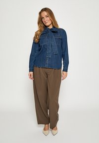 Džinsinė palaidinė su dideliu kaspinu prie apykaklės, dviem krūtinės kišenėmis, mėlynos spalvos, derinama su rudais klostuotais kelnėmis ir kreminėmis smailiomis aukštakulnėmis.