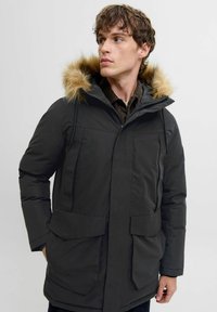 Sort polstret parka-jakke med en hætte foret med falsk pels, frontlynlås og to store udvendige lommer. Har et praktisk, isoleret design.
