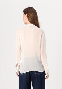 Kevyt, läpikuultava kermahuppari, jossa on pitkät hihat, kaulus ja sivuaukot. Pehmeä rakenne ja lentävä design, sopii kerrospukeutumiseen.