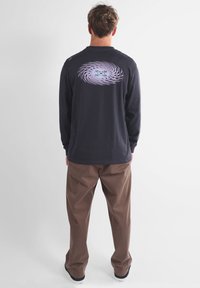 Chemise noire à manches longues avec un graphique en spirale violet dans le dos, assortie à un pantalon marron clair, dans un cadre simple.