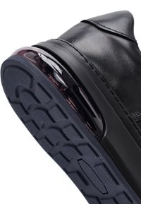 Suela de zapatilla de cuero negra con patrón de banda de rodadura profundo y almohadilla de aire visible en el área del talón, mostrada en un ángulo.