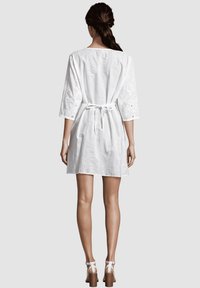 Vestido blanco de algodón con mangas de tres cuartos, atado en la cintura. Incluye detalles bordados en las mangas. Diseño con la parte trasera plana.