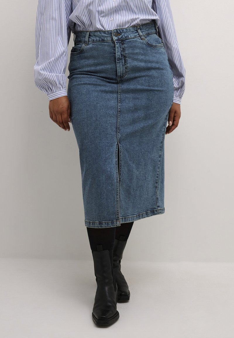 Lichtblauwe denim kokerrok met een voorknof en ritsluiting, en minimalistische stiksels. Gepaard met zwarte enkellaarsjes.