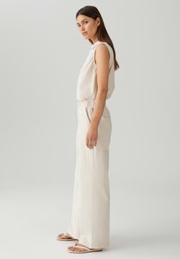 Lichtbeige mouwloze top gecombineerd met hoge taille, brede beige broek. Glad materiaal, elastische tailleband en eenvoudige sandalen.