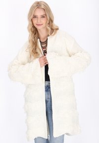 Vit stickad kofta med strukturerade vågiga mönster och överdimensionerade ärmar, med en öppen framsidan och en mysig look.