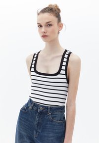 Canotta a righe bianco e nera in materiali a coste con scollo quadrato, abbinata a jeans in denim blu a vita alta.