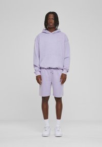 Lila Kapuzenpullover mit Kängurutasche und passenden lila Shorts. Hergestellt aus weichem Stoff; verfügt über eine lässige Passform und einen Kordelzugbund.