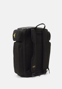 Črn nahrbtnik iz blaga z oblazinjenimi trakovi, večpredalno zasnovo in zlatim logotipom. Eleganten pravokoten oblik v gladki teksturi.