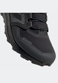 Černá turistická obuv s materiálem GORE-TEX, texturovaným syntetickým svrškem a robustní podrážkou s viditelnými trakčními výstupky.