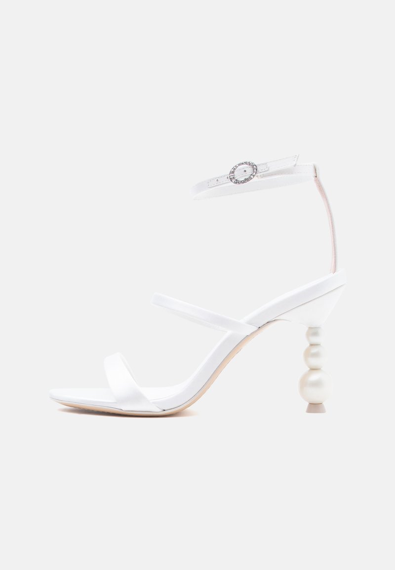 Λευκό σανδάλι με ψηλό τακούνι, λεπτά λουράκια, τακούνι σε σχήμα μαργαριταριού και αγκράφα αστραγάλου διακοσμημένη με στρας.