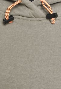 Sudadera de color gris claro con un tejido texturizado, que cuenta con cordones de ajuste en naranja y negro, y topes negros ajustables en el cuello.