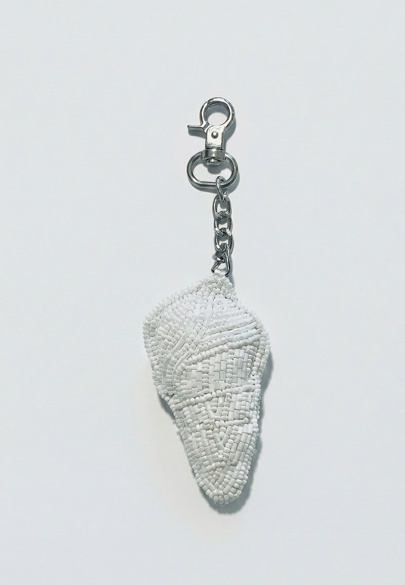 Porte-clés avec un fermoir en métal argenté attaché à un charme en forme de coquillage orné de perles blanches, suspendu sur un fond uni.