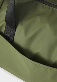 Sac à dos vert olive en nylon texturé, doté d'une fermeture éclair et d'une sangle noires. Le design comprend une poche ouverte spacieuse.