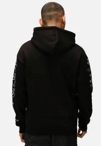 Felpa nera con tasca stile kanga, caratterizzata da grafiche bianche sulle maniche. Realizzata in morbido cotone, vestibilità rilassata.