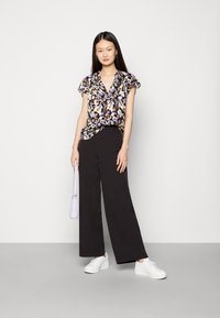 Blusa floral de mangas curtas em preto, branco, roxo e amarelo, combinada com calças largas de cintura alta pretas e ténis brancos.