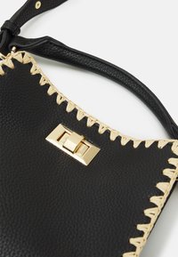Borsa a mano in pelle nera con accenti intrecciati naturali, dotata di una chiusura rettangolare dorata e cuciture decorative lungo i bordi.
