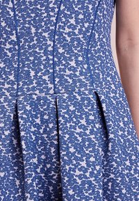 Robe bleue à motifs floraux avec un tissu texturé, comprenant des coutures ajustées et des plis à la taille pour une forme et un détail supplémentaires.