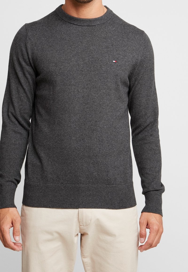 Pull en maille gris foncé avec un col rond, des poignets et un ourlet côtelés, avec un petit logo en rouge, blanc et bleu sur la poitrine.