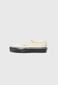 Canvas sneaker in off-white with black rubber sole. Features a low-profile design, rounded toe, and contrasting black outsole accents.