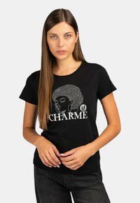 Maglietta nera in cotone, con una grafica del profilo di una donna e la parola "CHARME" in bianco. Maniche corte e scollatura rotonda.