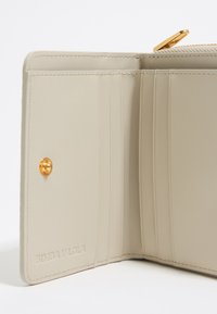Beige leren portemonnee interieur met meerdere kaartsleuven, gouden accenten en een gegraveerd logo. Soepele textuur en een strakke uitstraling. Ritssluiting.