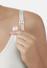 Weißes Bralette mit verstellbarem Träger, ausgestattet mit einem Kunststoffverschluss und einer weichen Stofftextur. Hand, die den Trägerversteller kneift.