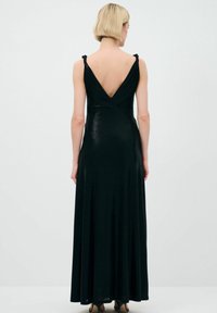 Schwarzes Abendkleid mit tiefem V-Ausschnitt im Rücken, dünnen verstellbaren Trägern und einem figurschmeichelnden Oberteil, das in einen ausgestellten Rock übergeht. Glatte Textur.
