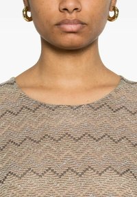 Top in tessuto dorato con motivo a zigzag. Il tessuto morbido presenta colori beige e bronzo. Girocollo e maniche corte. Orecchini a cerchio dorati.